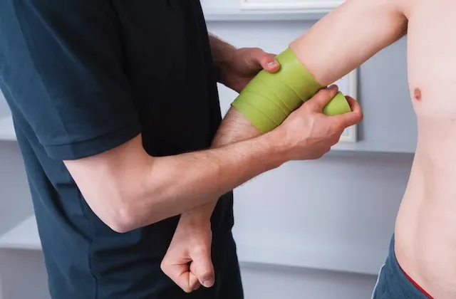Physiotherapeut führt eine Flossing-Behandlung am Arm eines Patienten durch, um die Durchblutung zu verbessern und die Mobilität zu fördern.